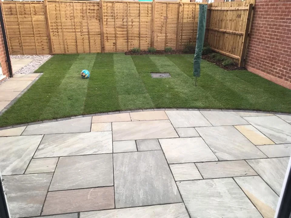 Backyard with a patio made of large stone slabs, a small grass area with a colorful ball, and a wooden fence surrounding the yard.