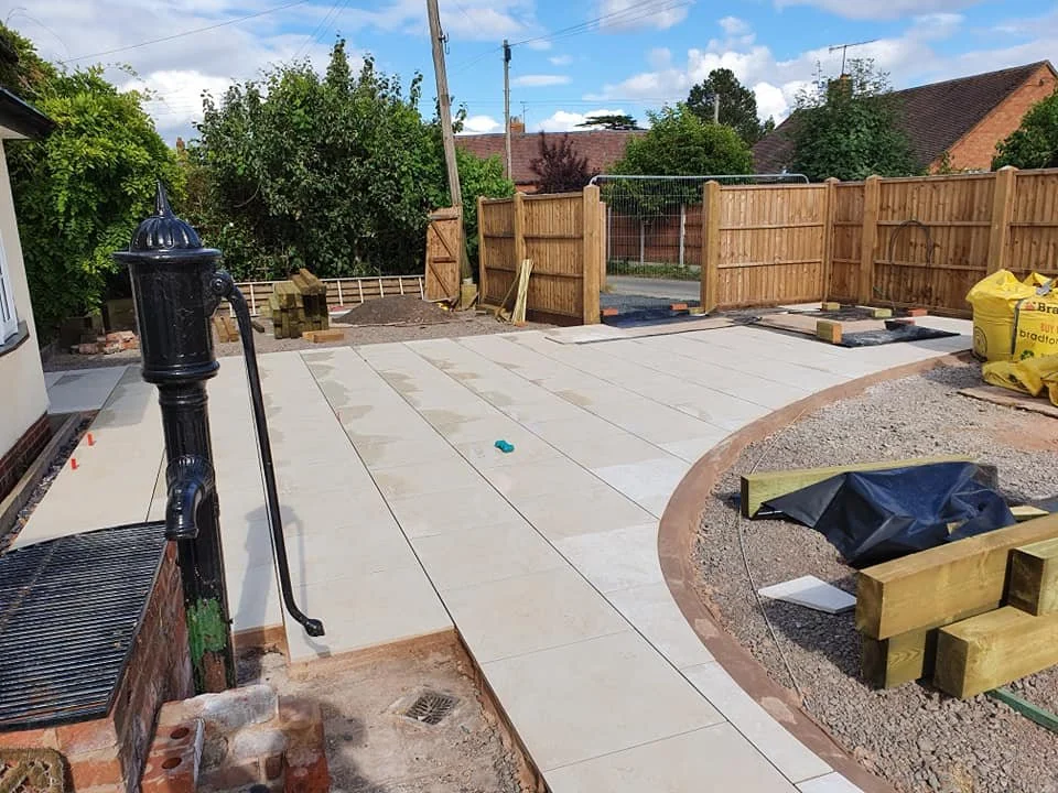 Backyard under construction with a partially completed concrete patio, wooden fence, and various construction materials.