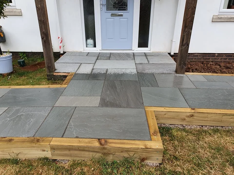 Newly installed gray stone walkway leading to front door of house, with wooden borders and grassy yard on sides.
