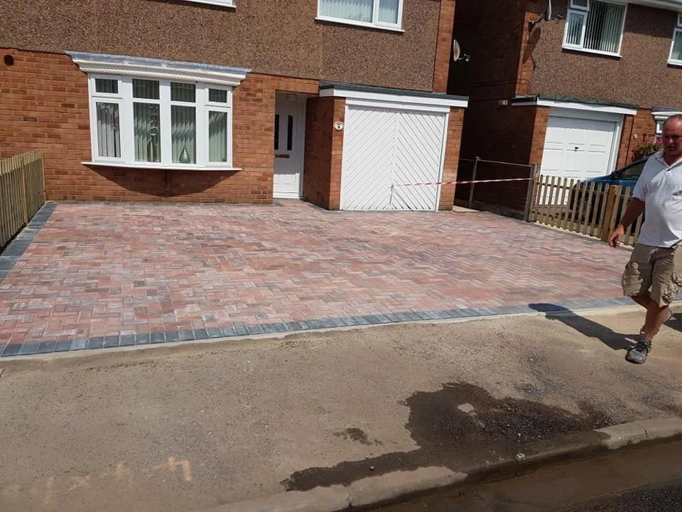 Newly paved brick driveway in front of a house with a window and garage, and a man walking past.