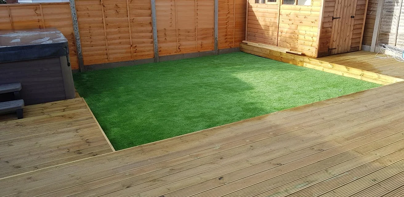 Backyard with wooden deck, artificial grass, wooden privacy fence, and a hot tub.