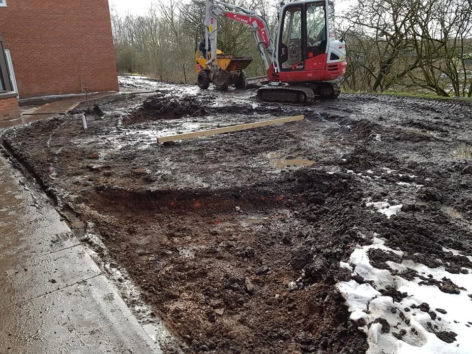 Construction site with excavator digging soil near a building, with snow on the ground.