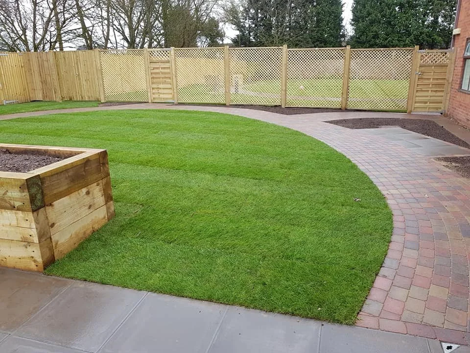 Backyard with a curved brick patio, a grassy area, a wooden planter box, and a wooden fence.