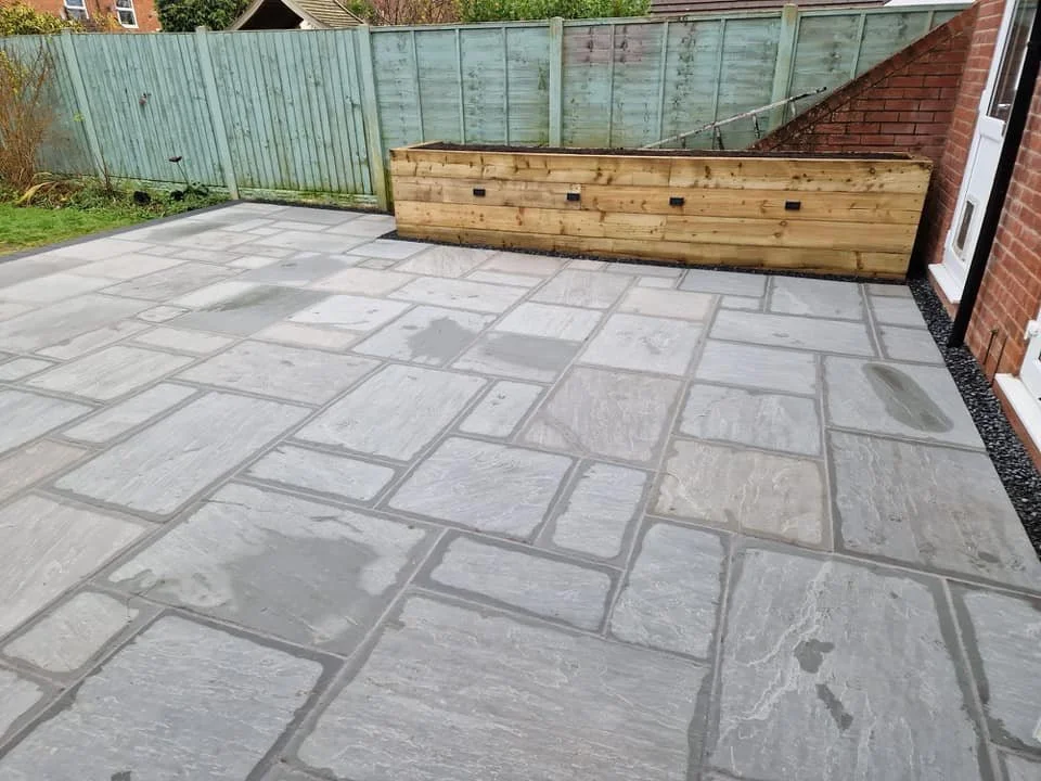 A newly paved stone patio with a wooden fence and brick wall near a white door outside.