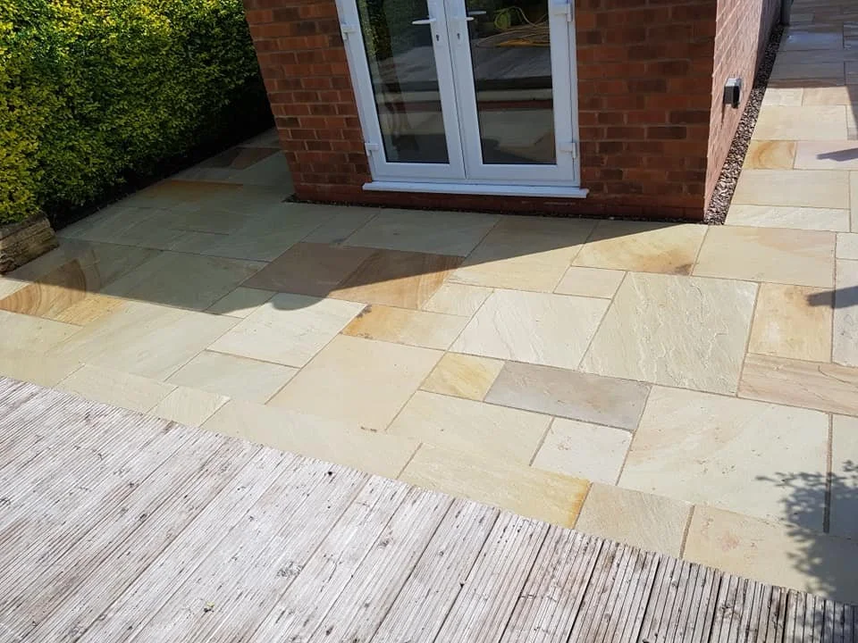 Newly paved beige and cream stone patio outside a brick house with a glass door.