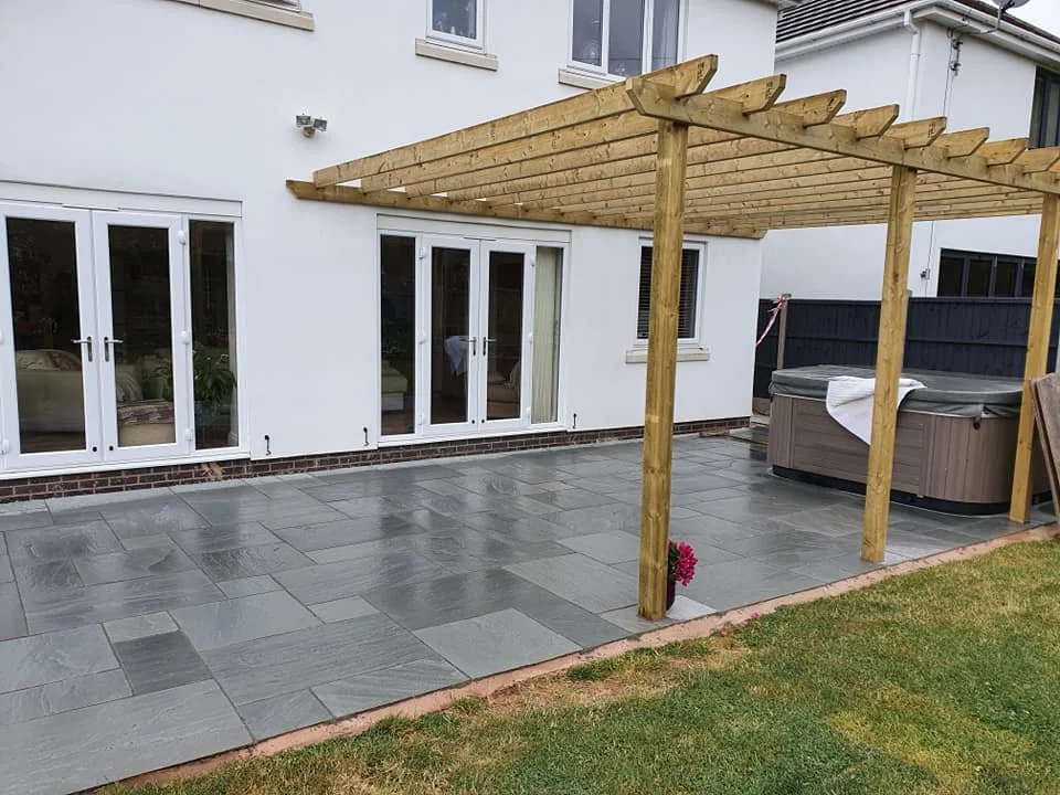 Backyard patio with a newly constructed wooden pergola, sliding glass doors, hot tub, and small potted plant.
