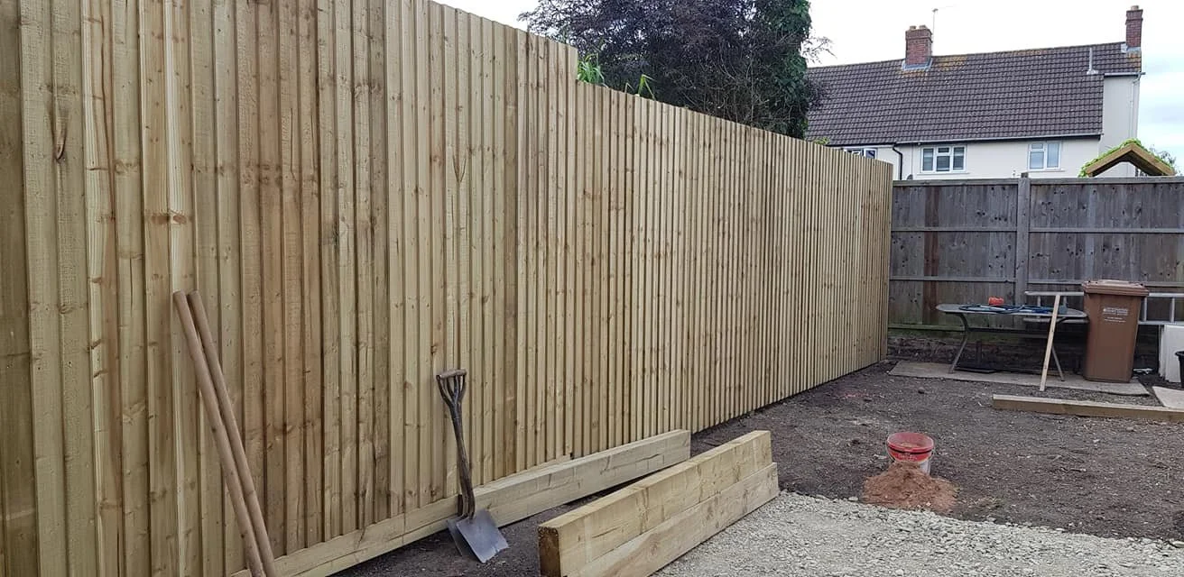 A backyard with ongoing fence construction, new wooden panels, a shovel, a level, and construction supplies.