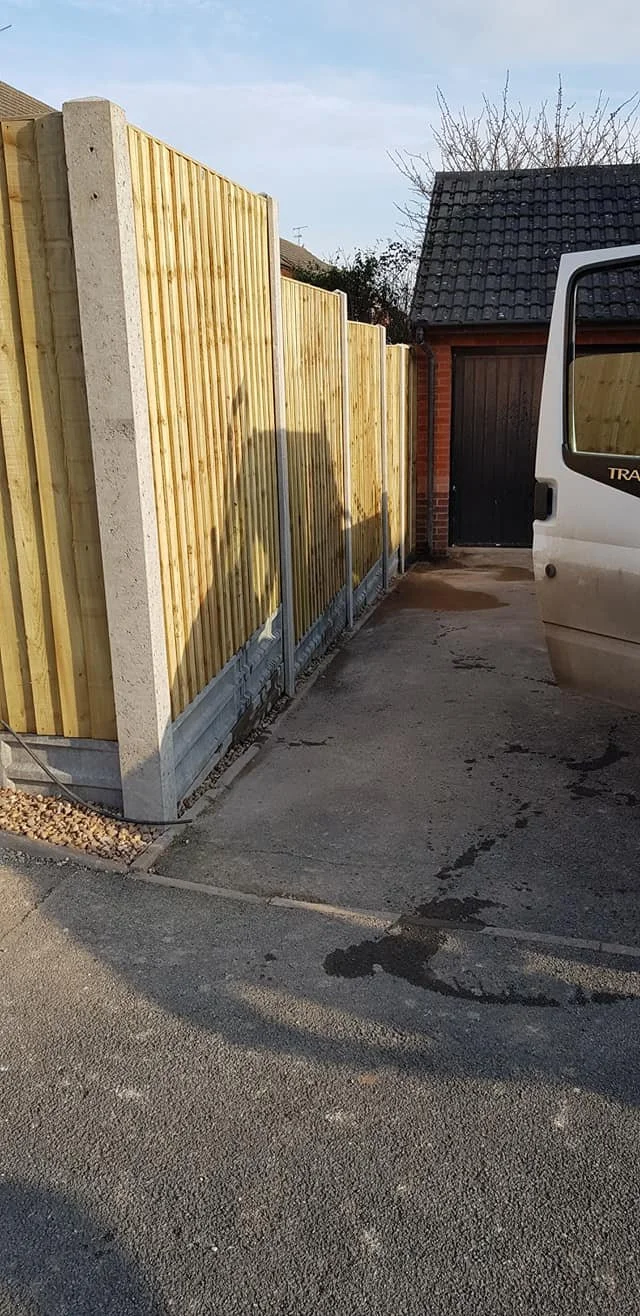 Residential driveway with a new wooden fence, a black garage door, and part of a white van on the right side.