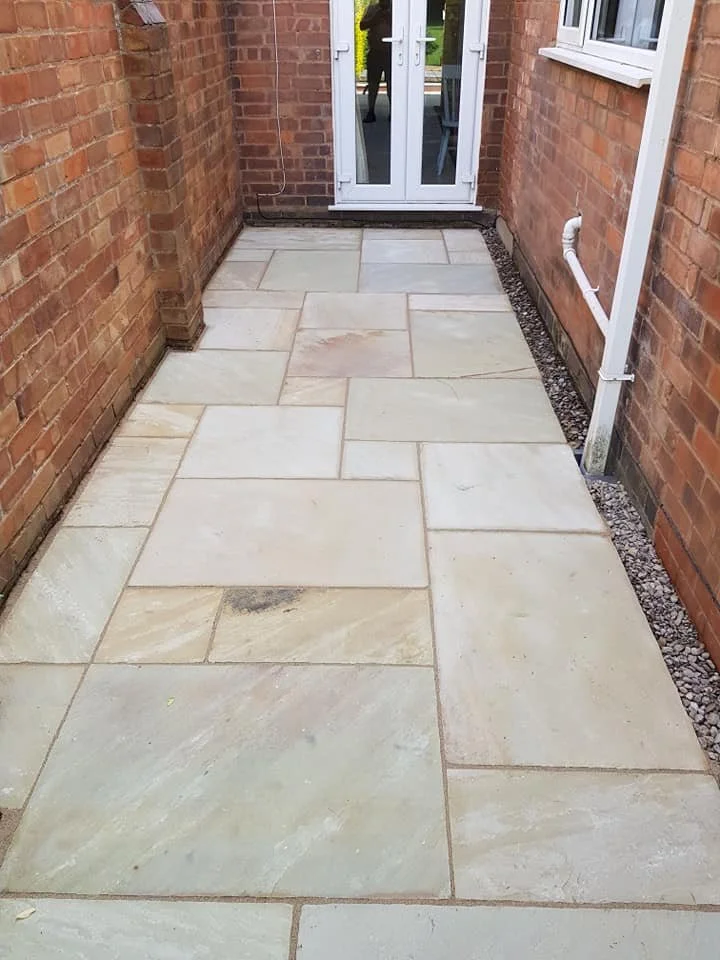 Clean beige stone patio with a white framed glass door and brick walls.