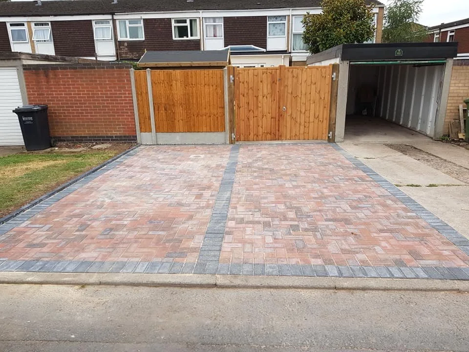 A paved driveway with two parking spaces separated by a border, leading to a wooden gate and a garage on a residential property.