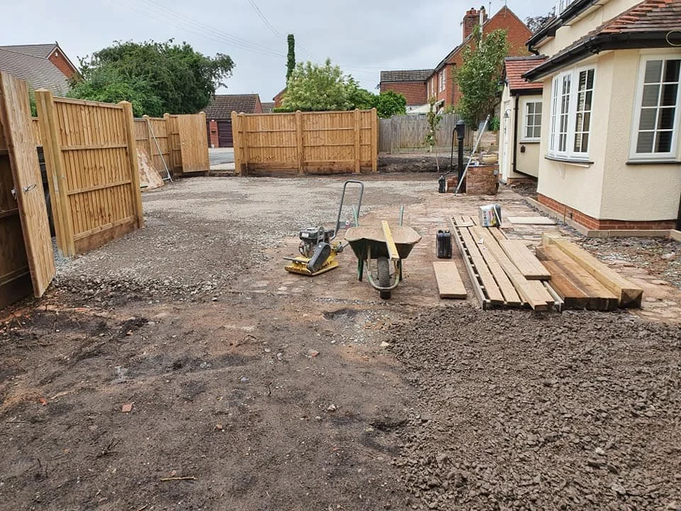 Backyard under construction with wooden fencing, paving stones, a wheelbarrow, and construction tools.