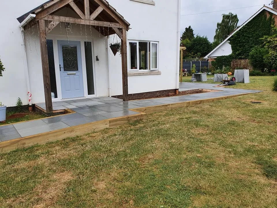 Backyard with newly laid stone patio and small garden bed with grass.