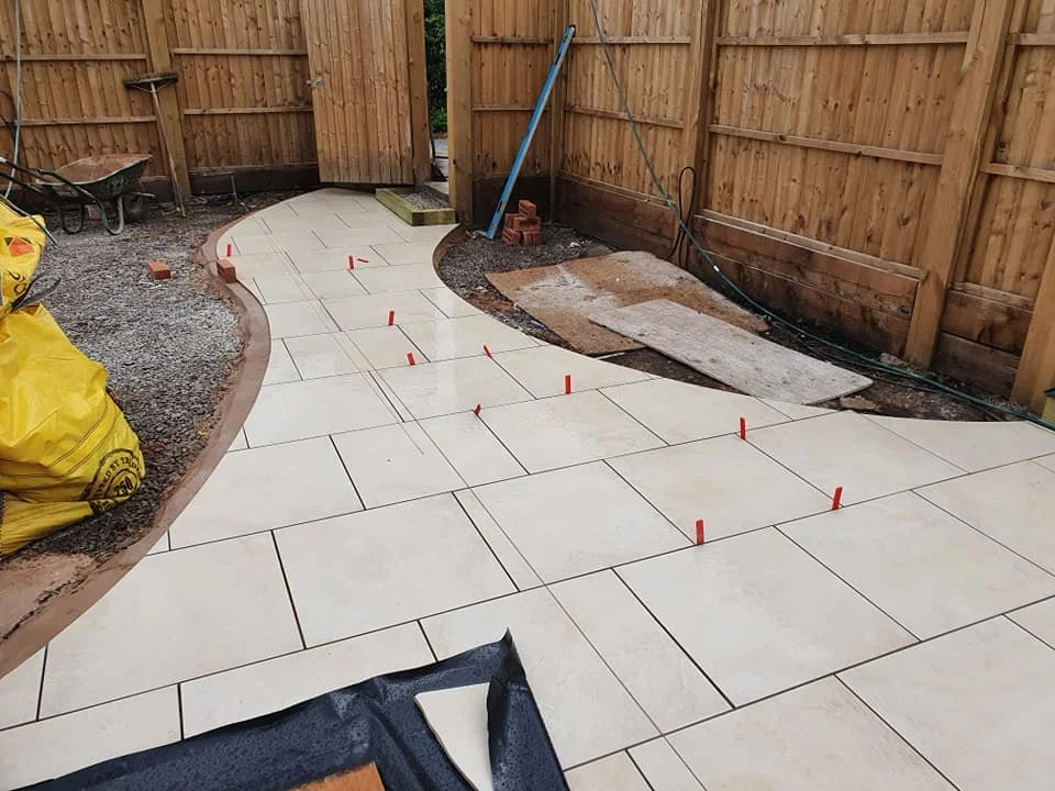Under construction, light-colored paving stones being laid in a curved pattern within a fenced backyard.