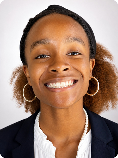 Close-up of a smiling African American woman with natural hair and hoop earrings, wearing a blazer and white blouse against a neutral background.