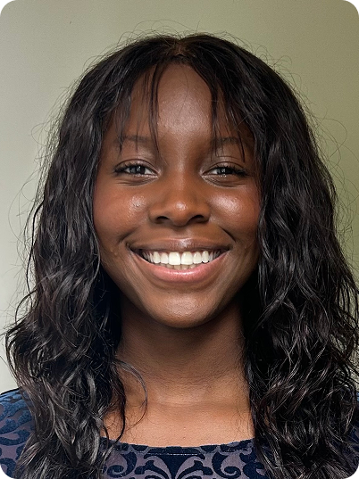 A young woman with a big smile, long curly black hair, and wearing a patterned dark blue top.