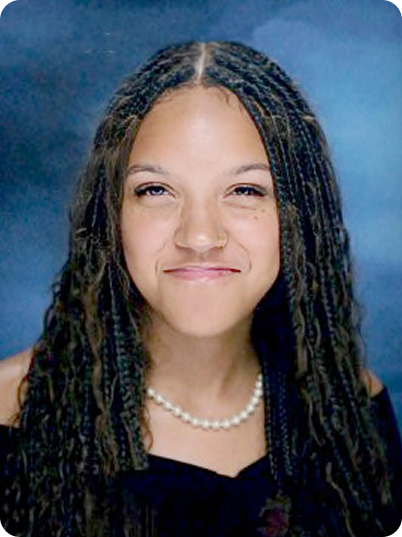 Young girl with long curly hair and a pearl necklace, smiling and winking, in a school photo with a blue background.