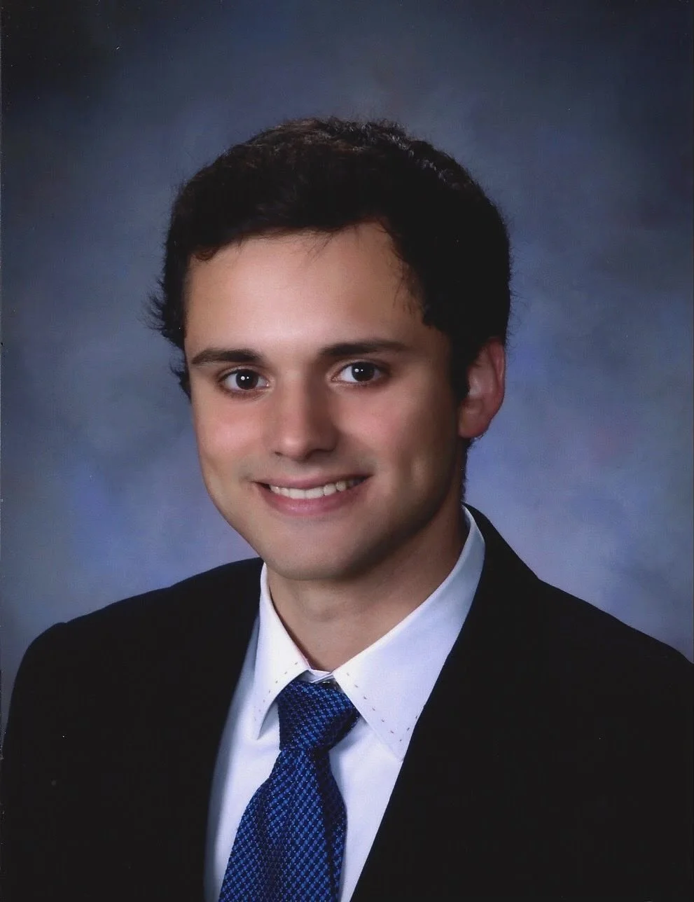 A young man in a formal suit and tie smiling for a portrait.
