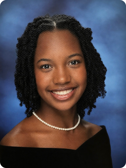 Portrait of a young African American woman with natural curly hair, smiling, wearing a pearl necklace and a black top against a blue background.