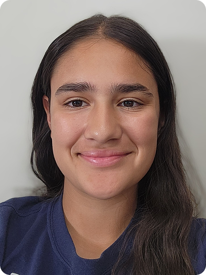 Close-up of a young woman with long dark hair, smiling, wearing a dark blue shirt, against a plain light-colored background.