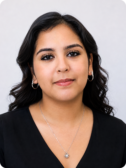 Close-up portrait of a young woman with dark hair wearing a black top, hoop earrings, and a silver necklace, against a light background.