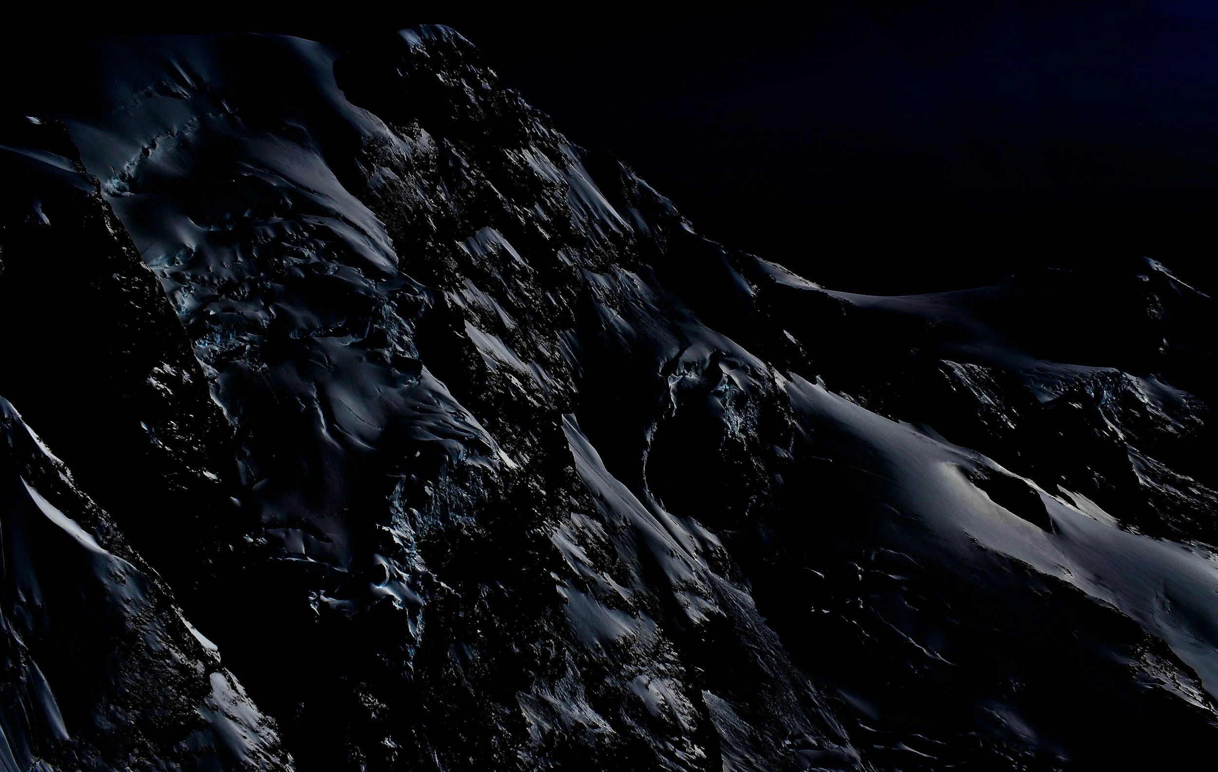 Dark, snow-covered mountain peaks under a black sky.