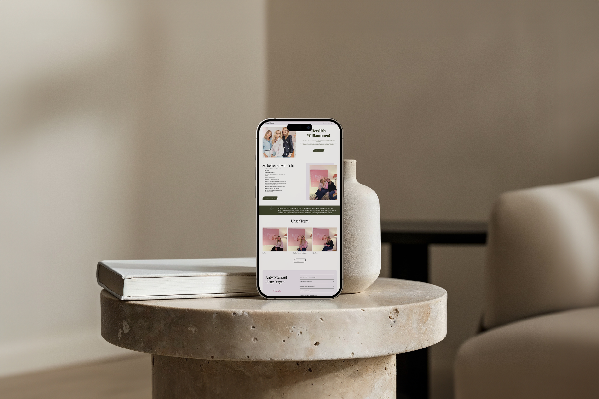 Smartphone auf einem runden Steintisch zeigt eine Webseite mit Frauen und Texten in deutscher Sprache.