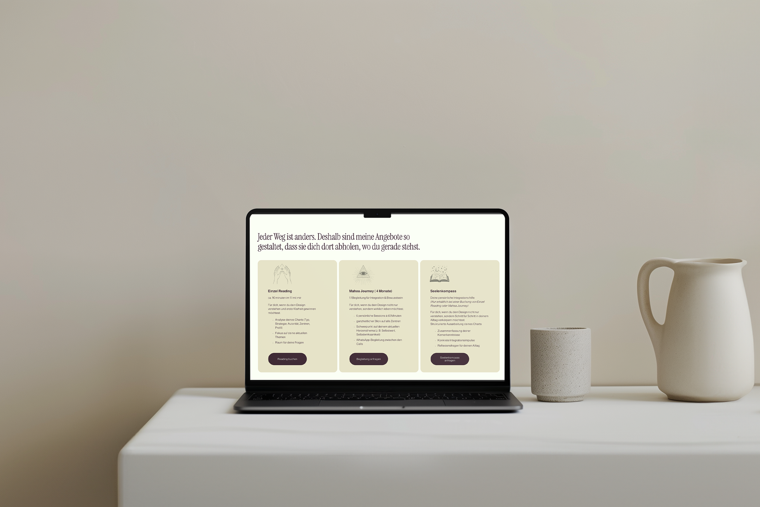 Ein Bildschirm zeigt eine Webseite in deutscher Sprache mit Angeboten für persönliche Entwicklung und Achtsamkeit, auf einem weißen Tisch neben zwei weißen Keramikvasen und einem Becher. Der Hintergrund ist neutral und schlicht.