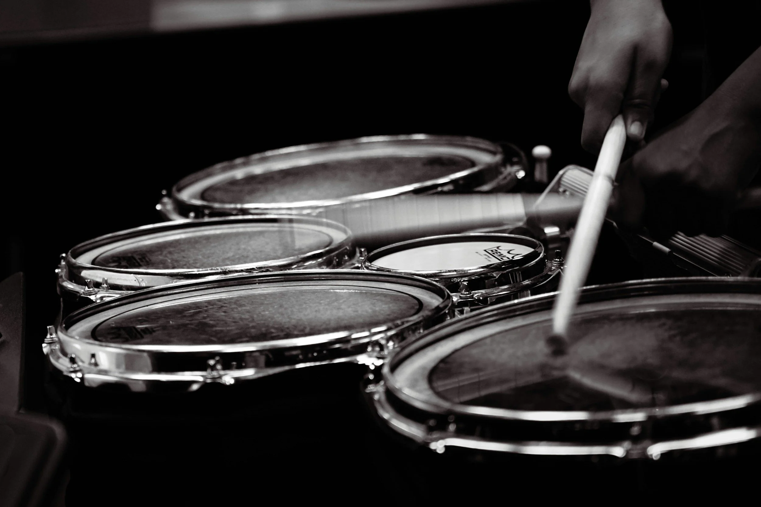 Close-up of a person's hand playing a drum set with drumsticks, black and white photo