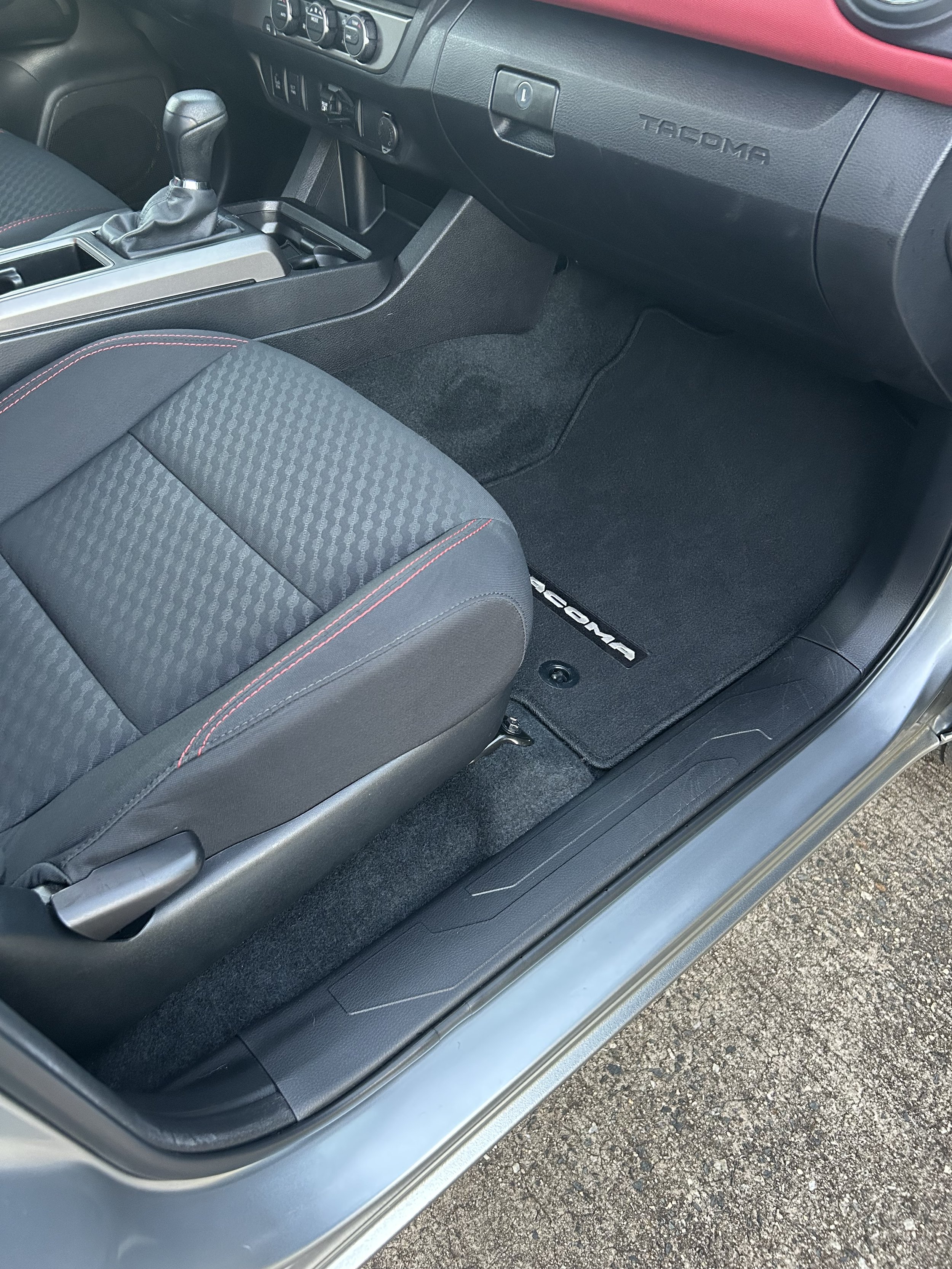 Interior of a Toyota Tacoma vehicle, showing the passenger side floor mat, seat, and parts of the dashboard and center console.
