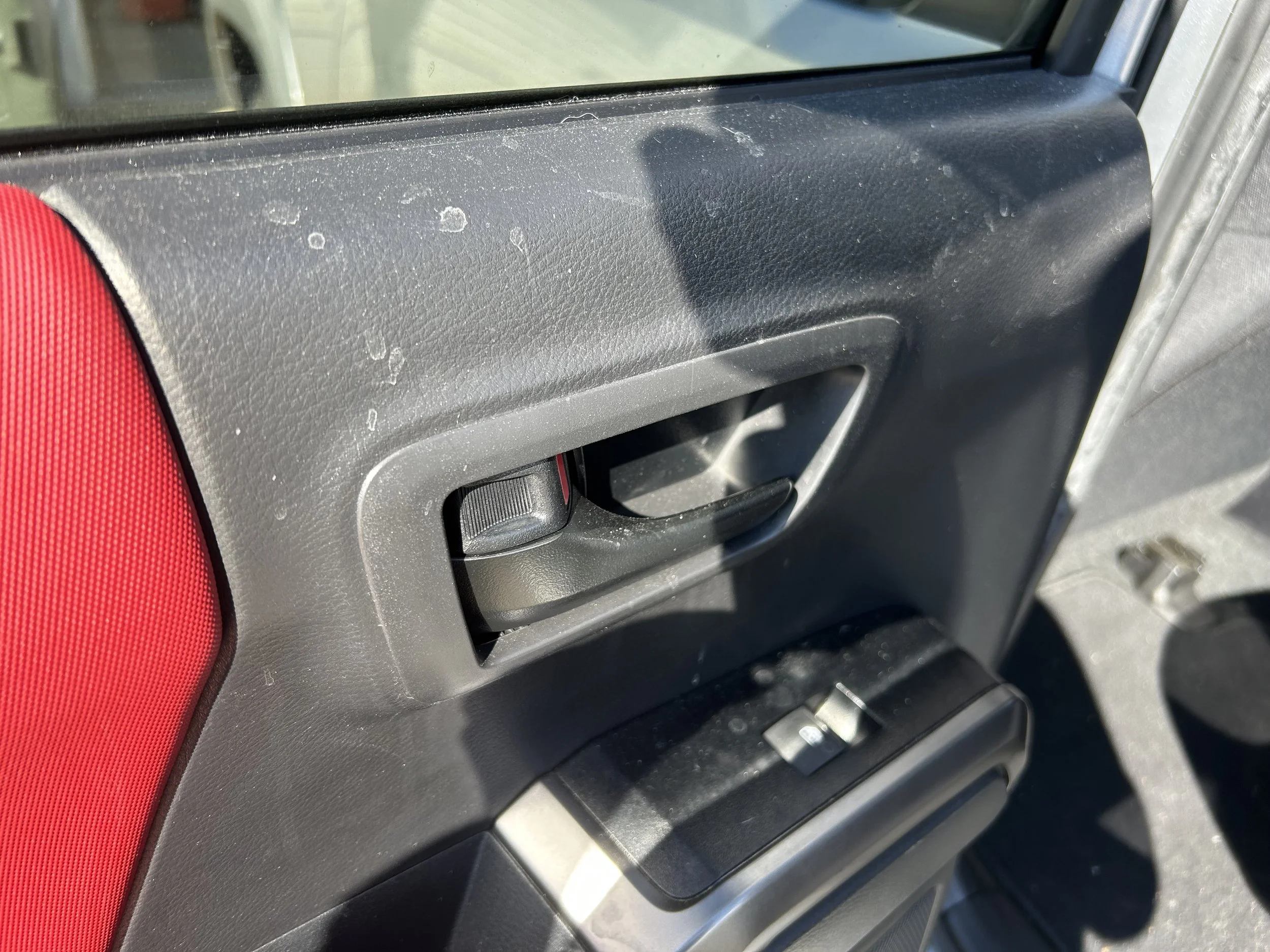 Car door interior with black plastic panel, window control switch, and red fabric accent.