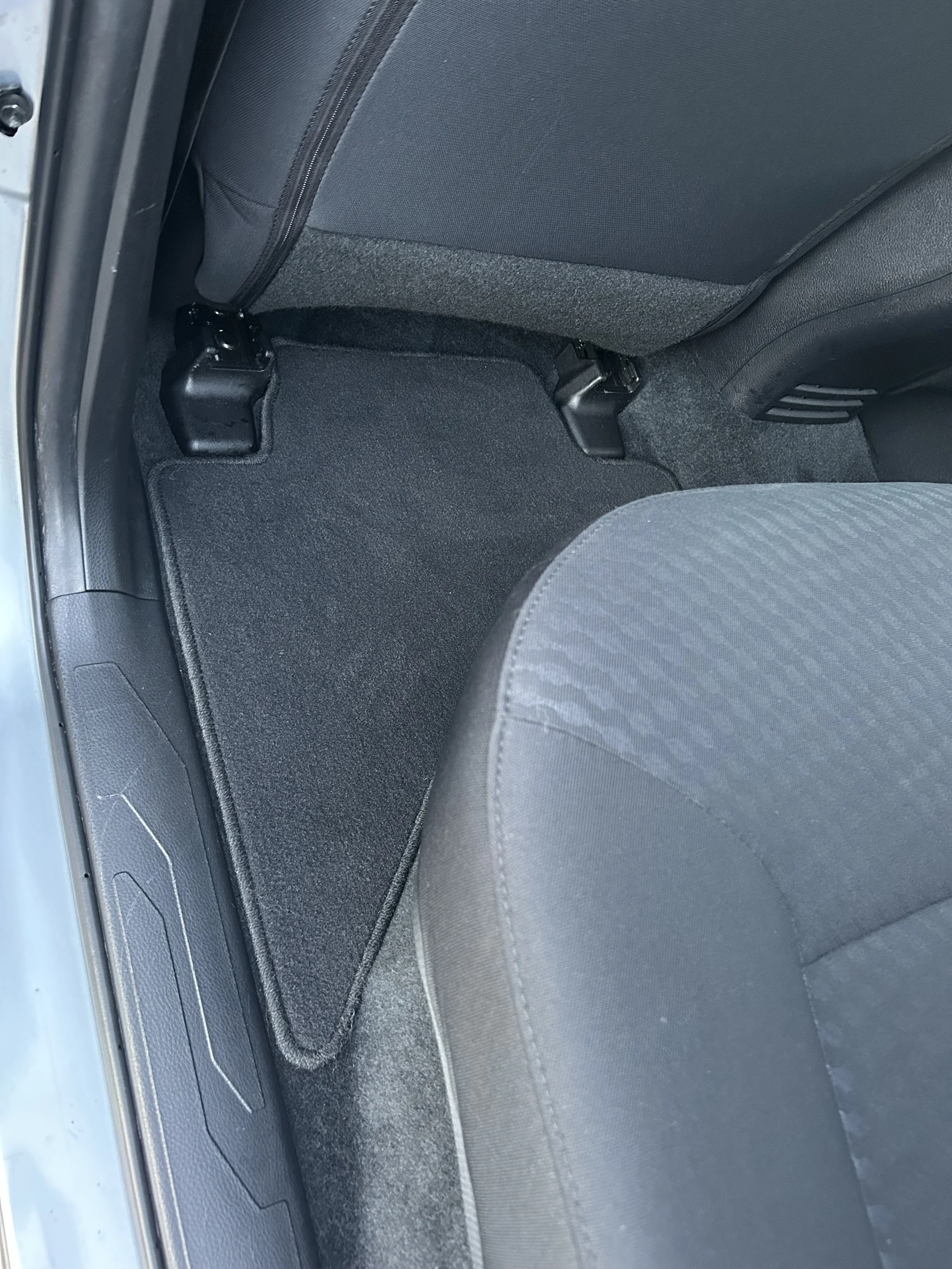Car interior showing the back seat area with a black floor mat, grey fabric seat, and part of the car door.