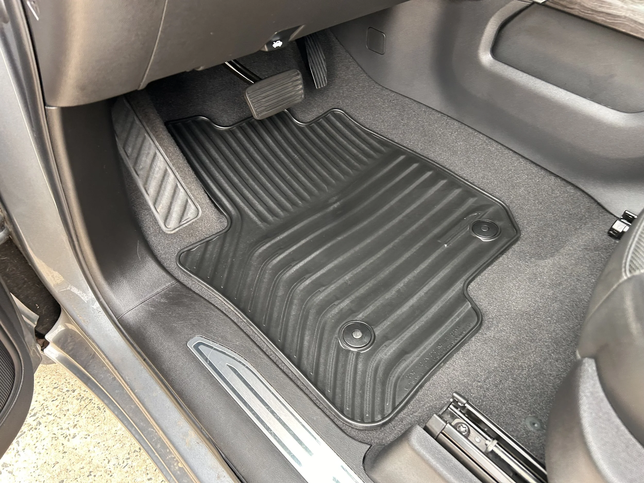 Black rubber car floor mat in the driver's side footwell, with the accelerator and brake pedals visible.