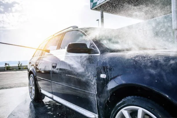 Black station wagon car being washed with water and a spray nozzle at a car wash station.