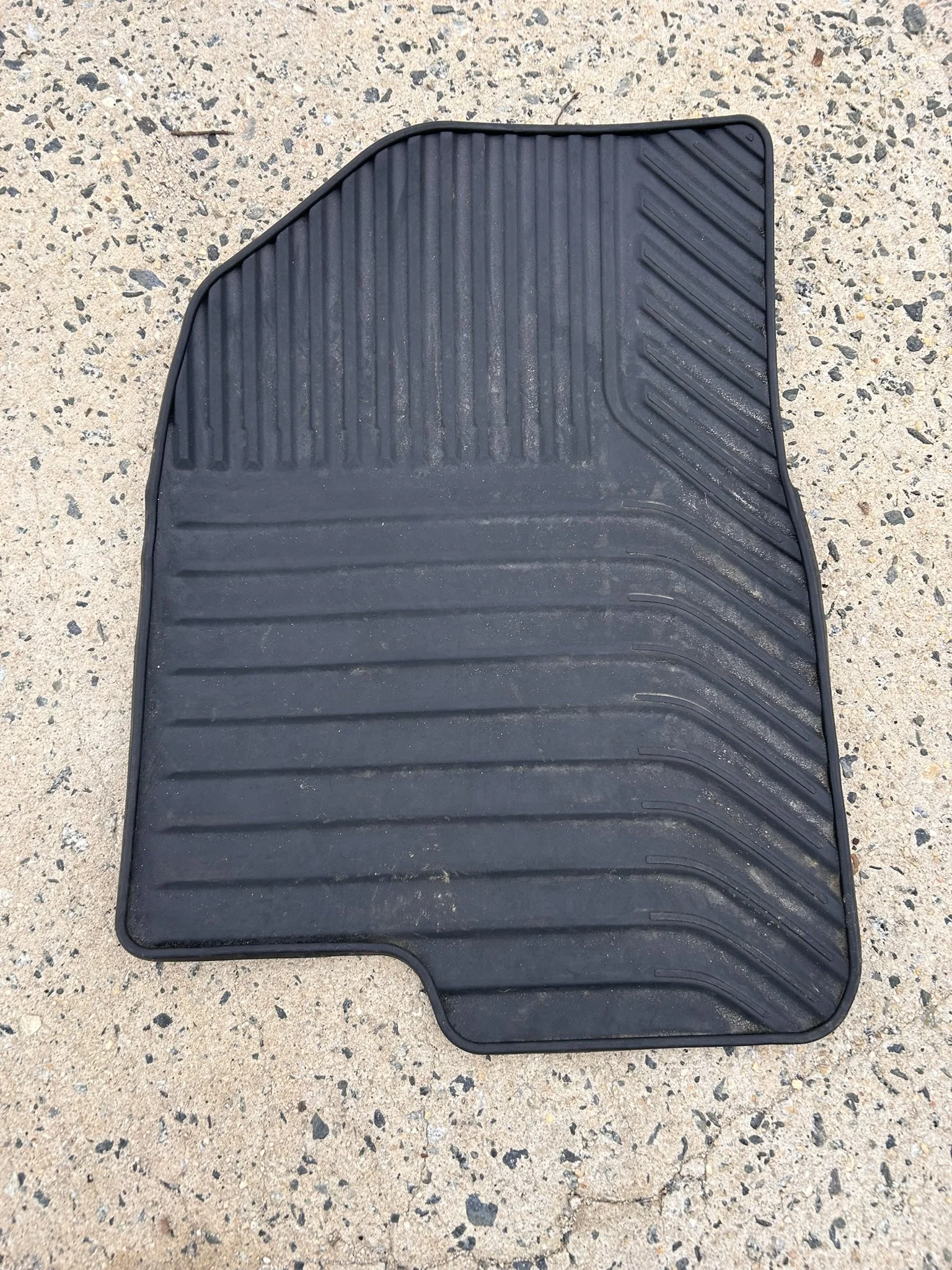 Black rubber car floor mat with textured surface, placed on concrete ground.