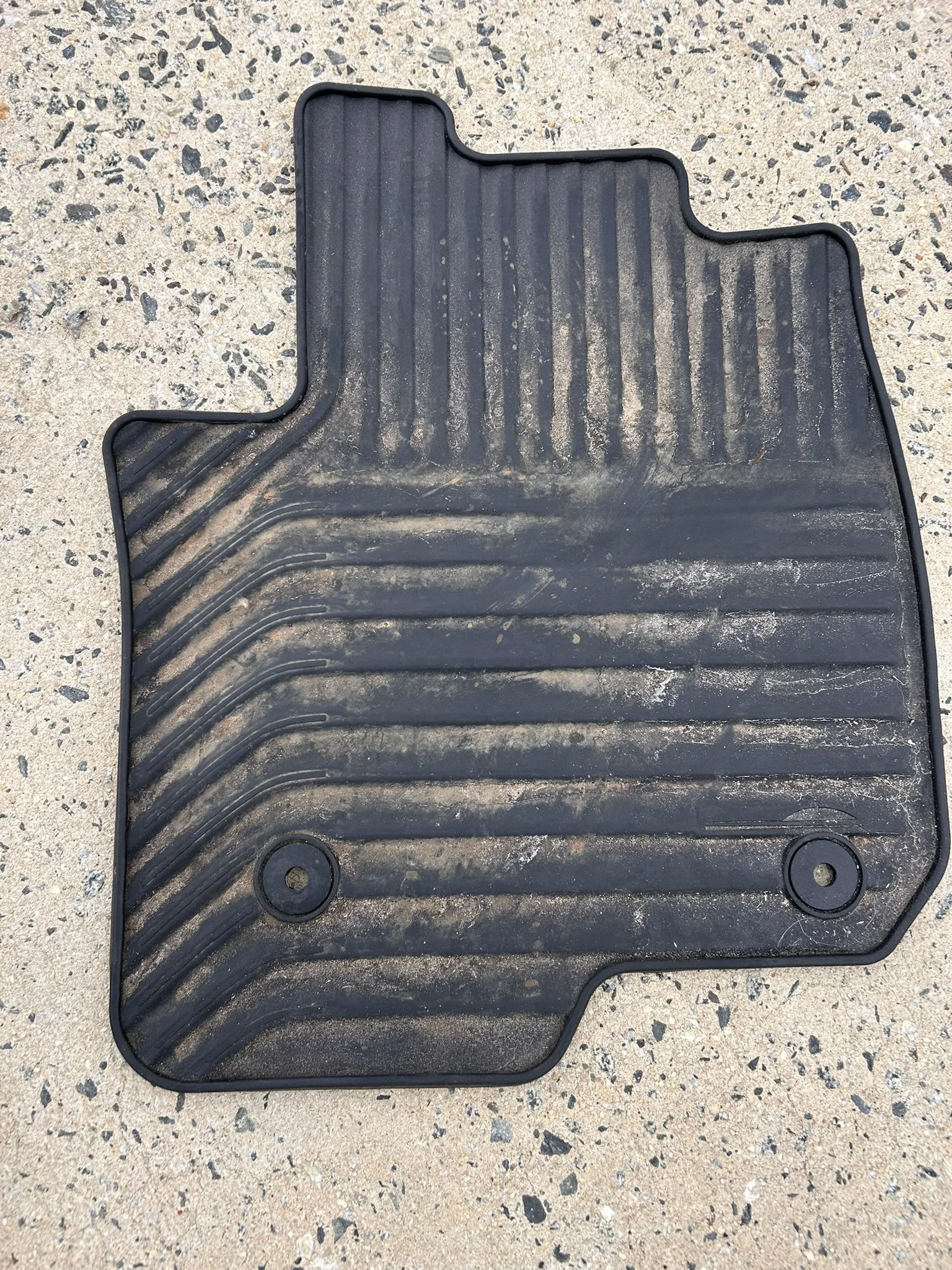 Black rubber car floor mat with dirt on a concrete surface.