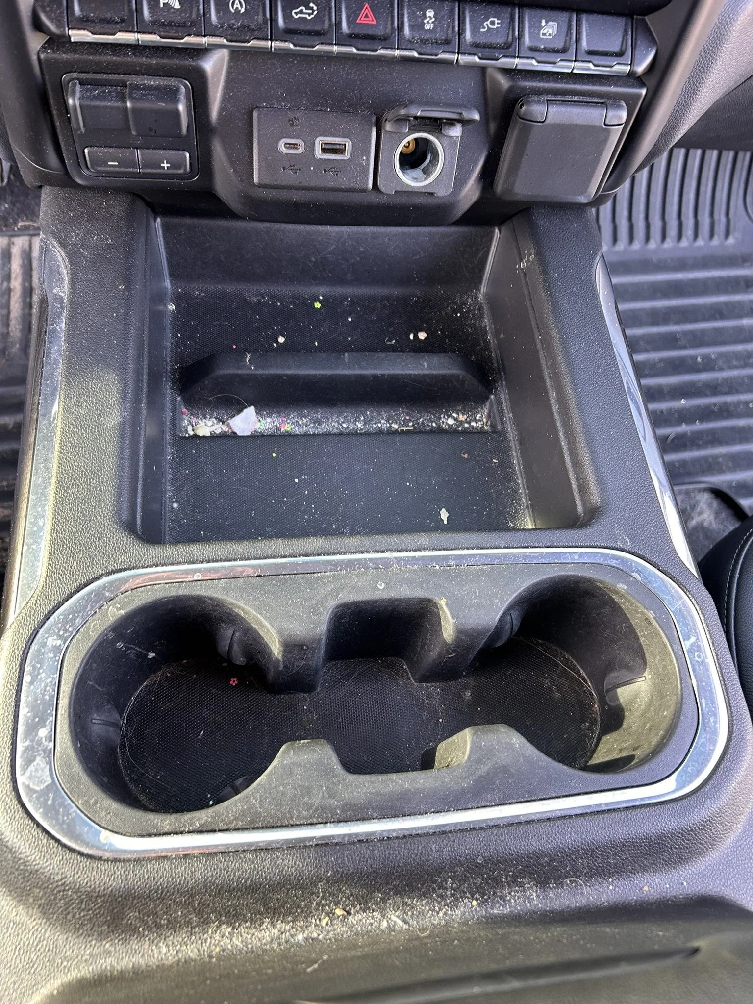 Dirty car cup holders and center console with trash and debris.
