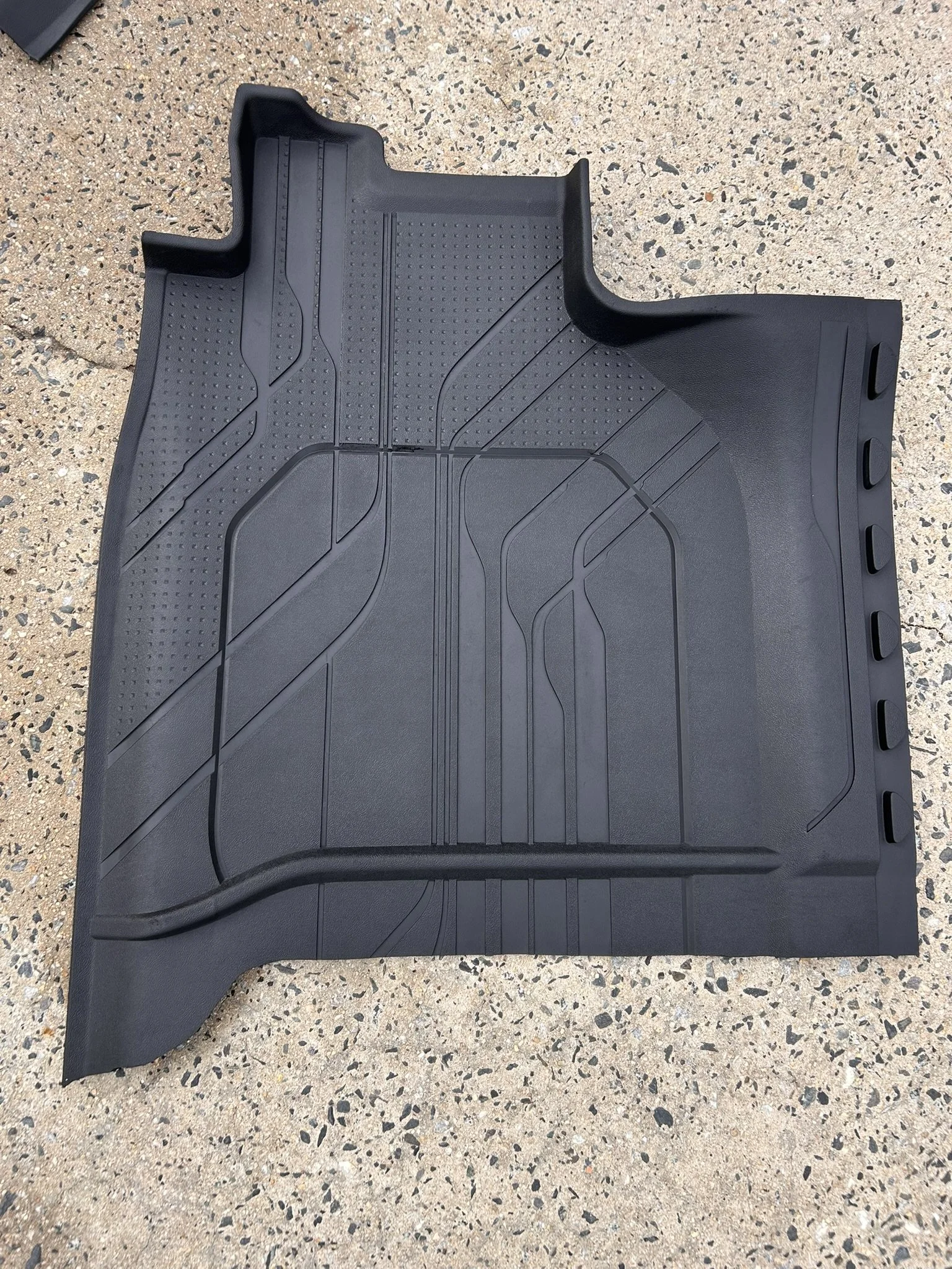 Black rubber car floor mat on speckled concrete surface.