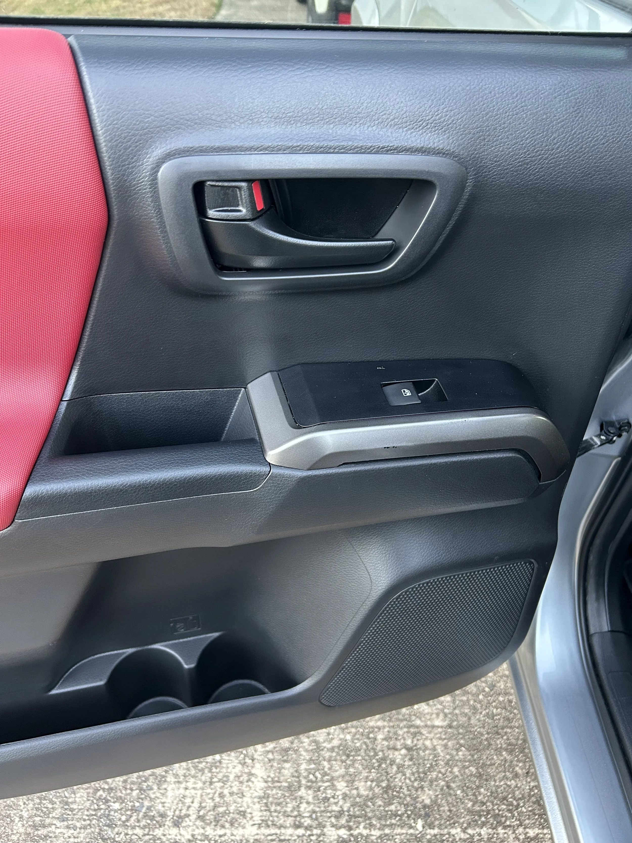 Close-up of a car door interior showing a black door handle, window lock switch, storage compartment with cup holders, and speaker grille.