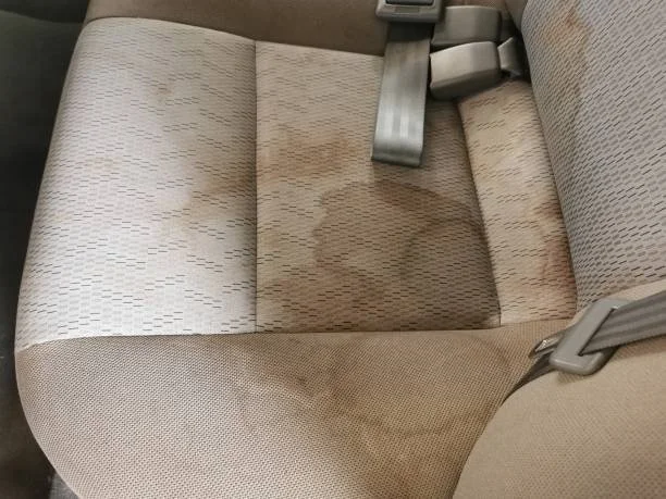 Car back seat with wet stain, showing fabric and seat belts.