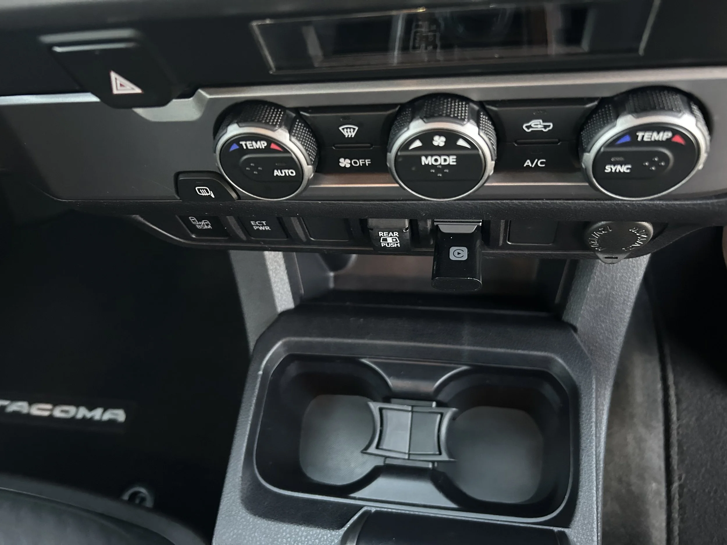 Center console and dashboard of a Toyota Tacoma vehicle, showing climate controls, cup holder, and gear shift area.