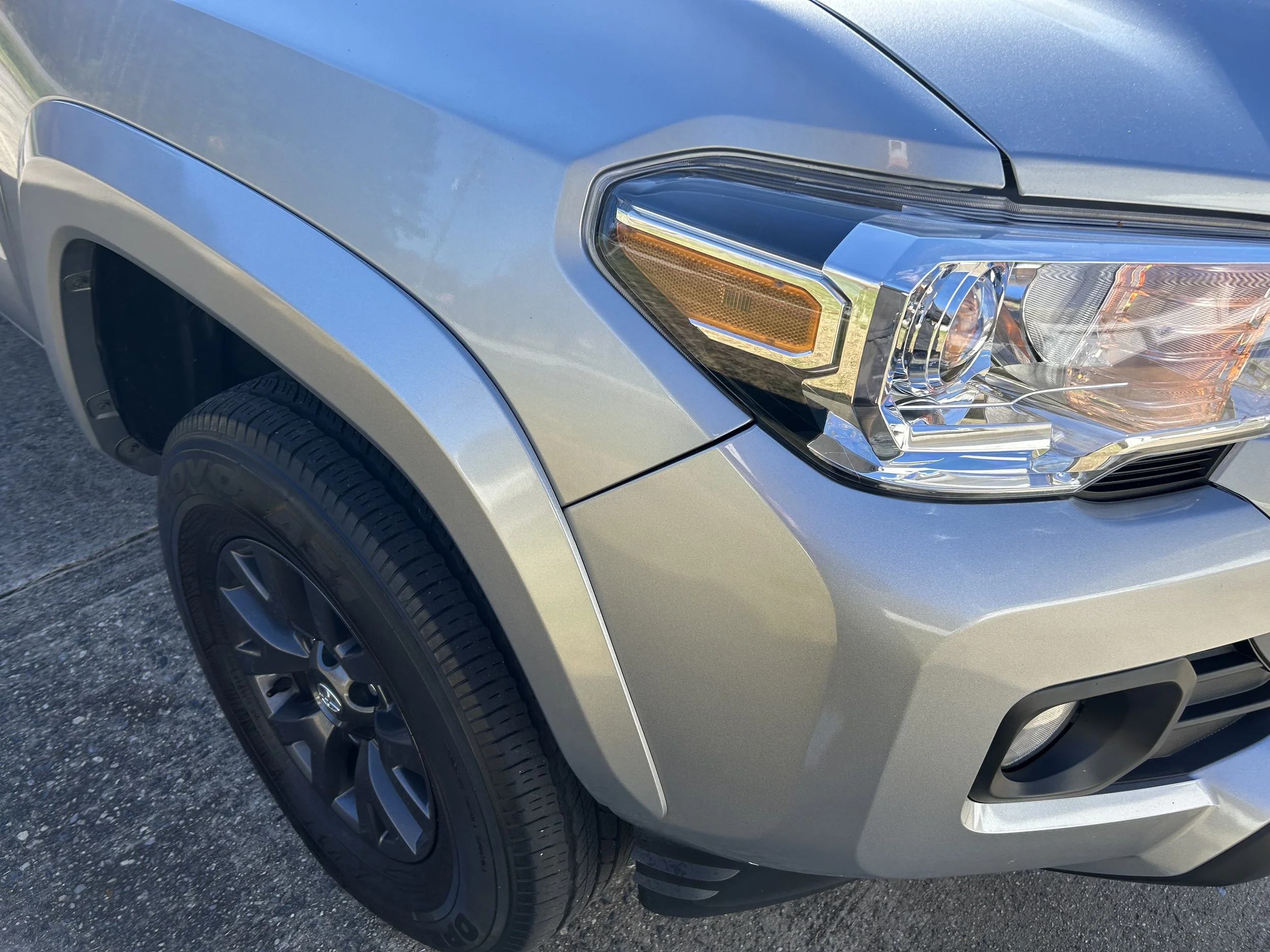 Silver SUV front left corner showing headlight, wheel, and part of the hood.