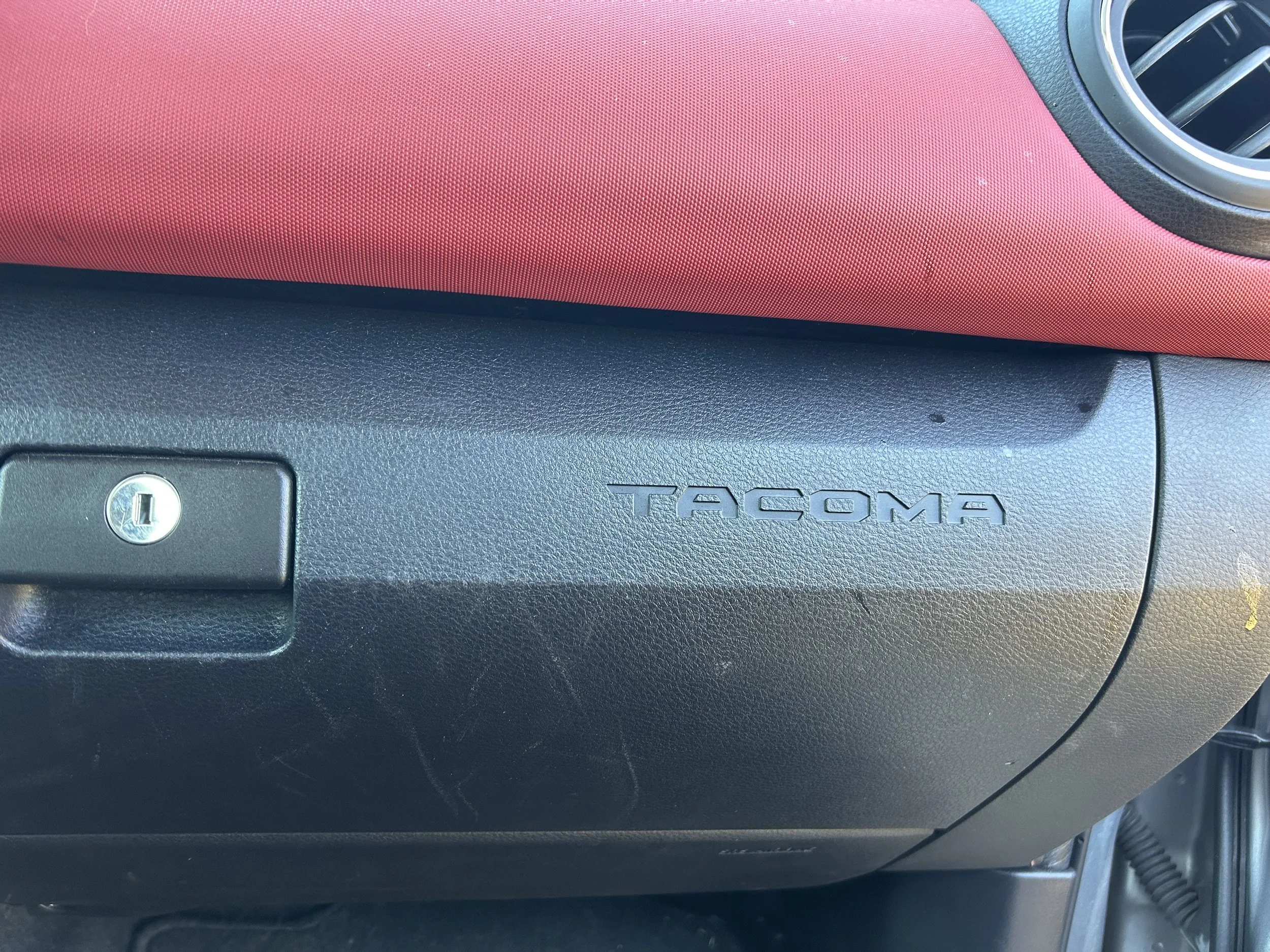 Close-up of the dashboard of a Toyota Tacoma, showing the red and black interior.
