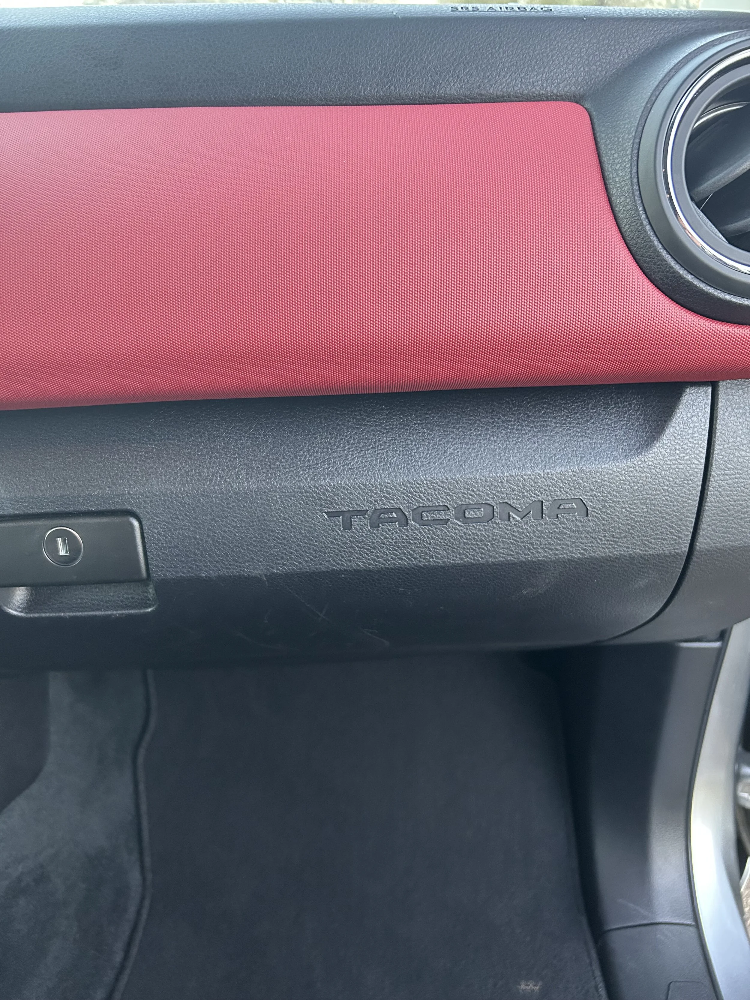 Interior of a Toyota Tacoma truck dashboard with a red panel and air vent.