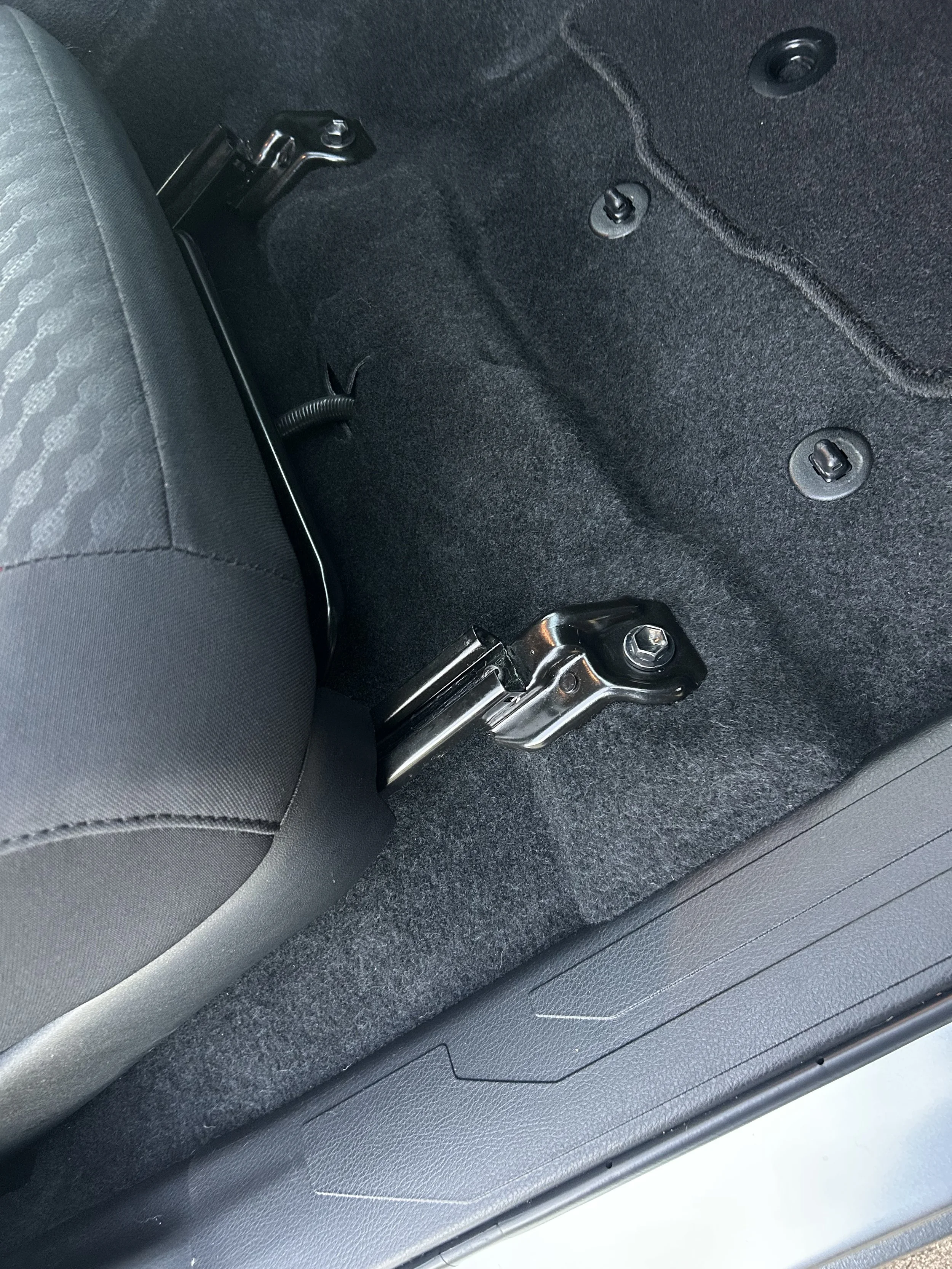 The interior of a car showing the rear seat and floor area, with visible hardware and mounting points for the seat, and some carpeting and trim.