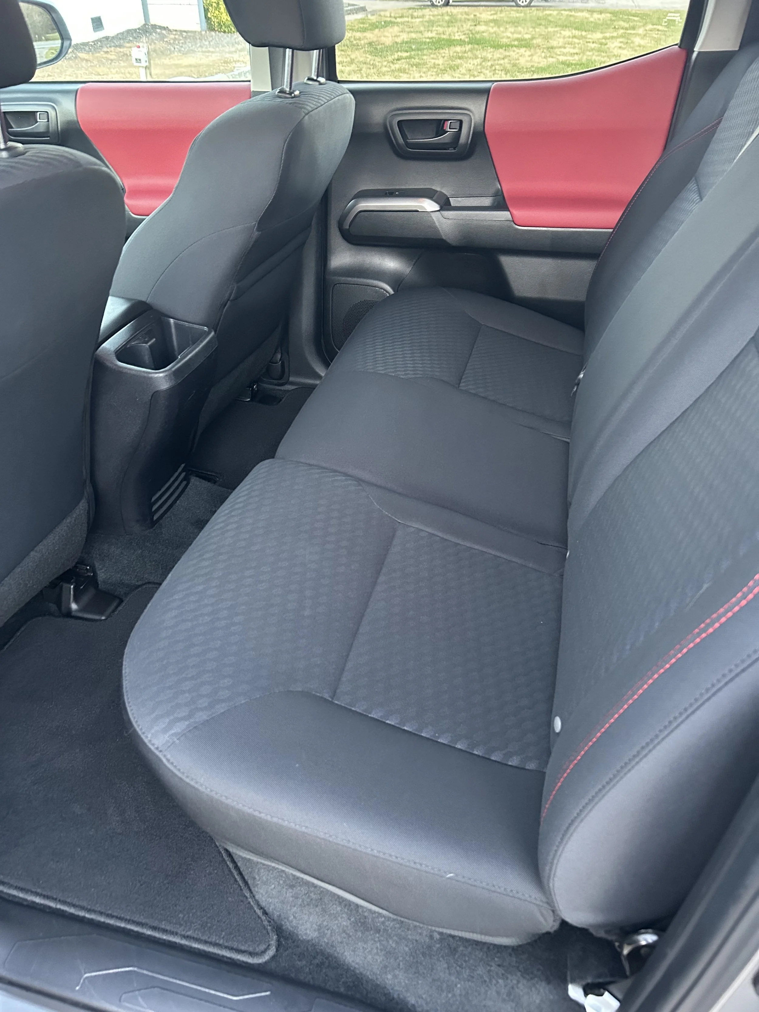 The interior of a vehicle showing the backseat area with black fabric seats, a black door panel with a red accent, and a view of the front seats and dashboard.