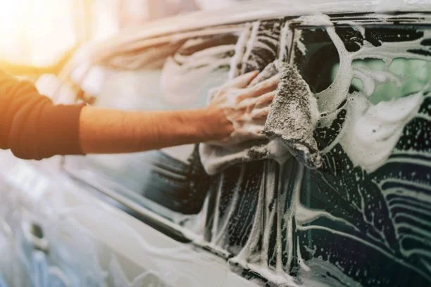 Person cleaning a black car with soap and sponge during washing.