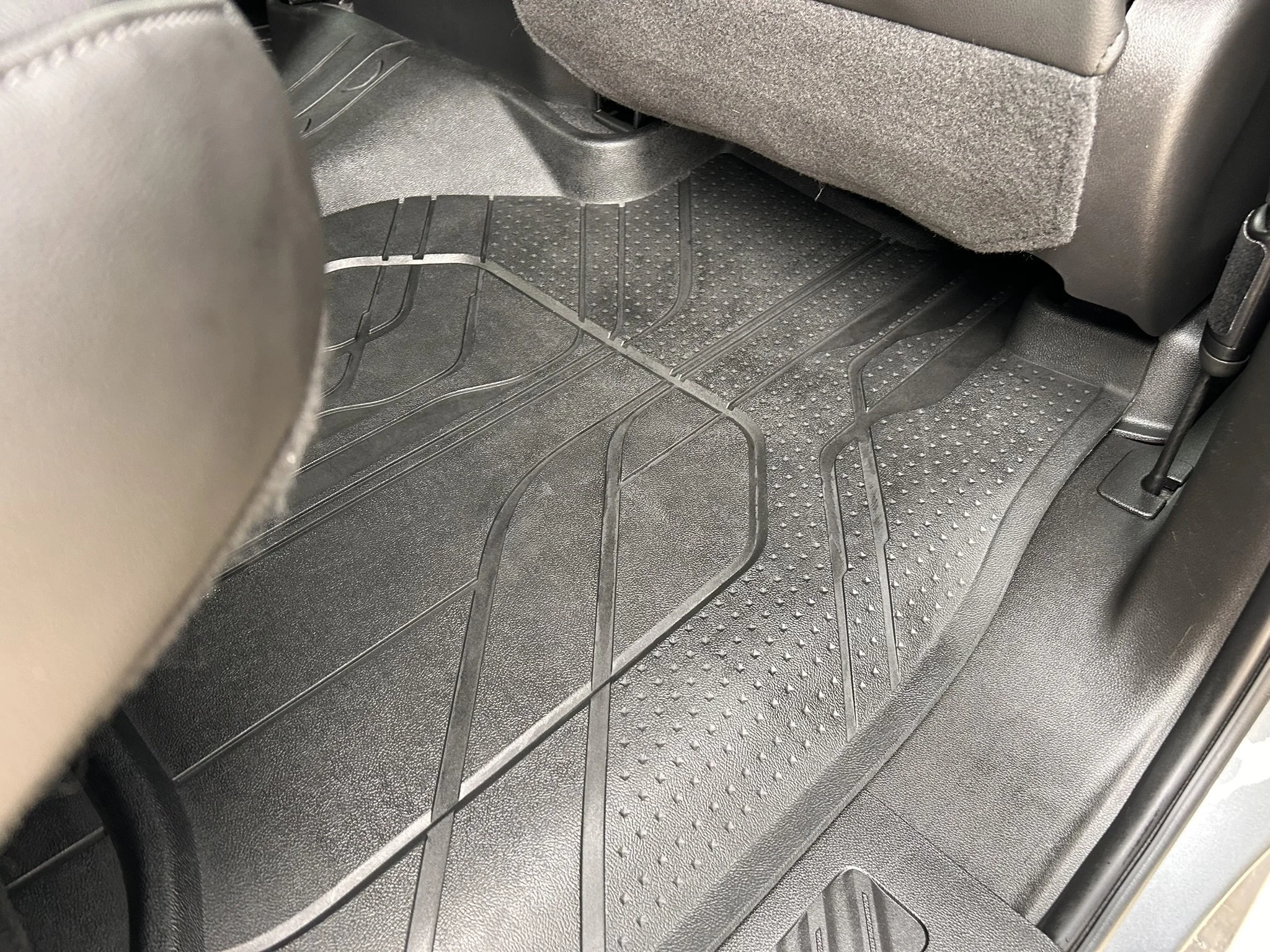 Black rubber car floor mat with textured surface and raised edges, fitted on the vehicle's floor behind the front passenger seat.
