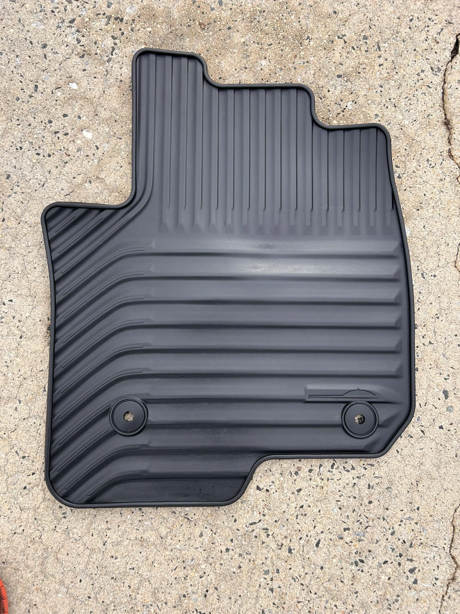 A black rubber car floor mat with ridges, placed on concrete ground.