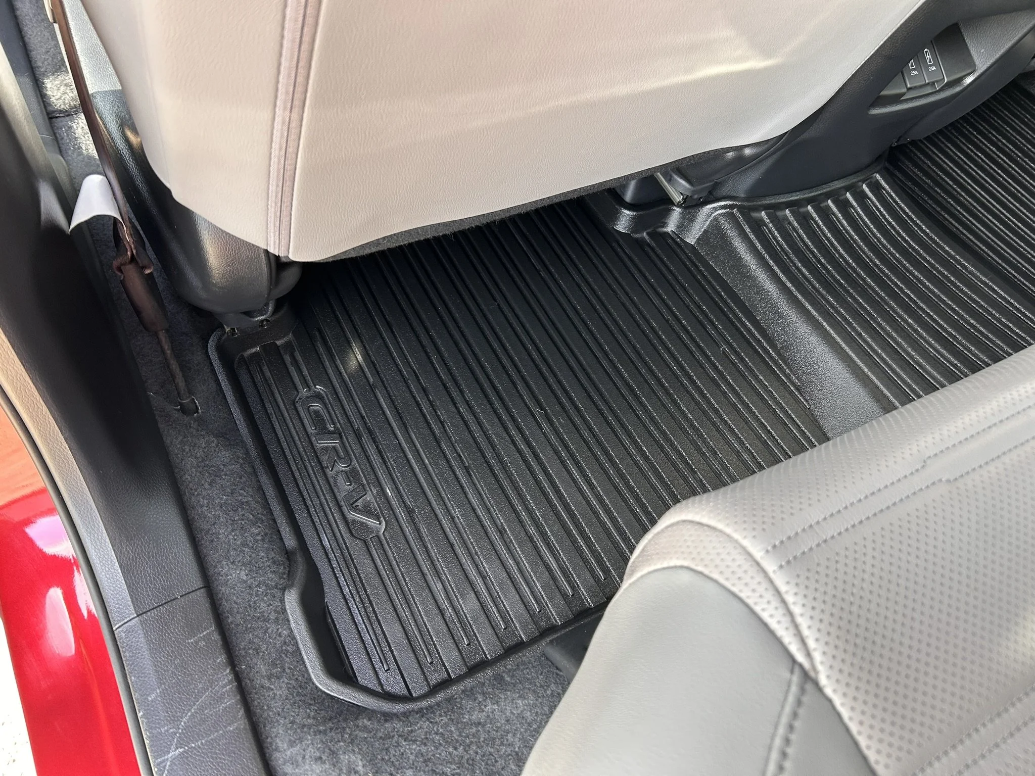 The interior back seat area of a car showing a black rubber floor mat with ridges, beige seat back, and a gray seat.