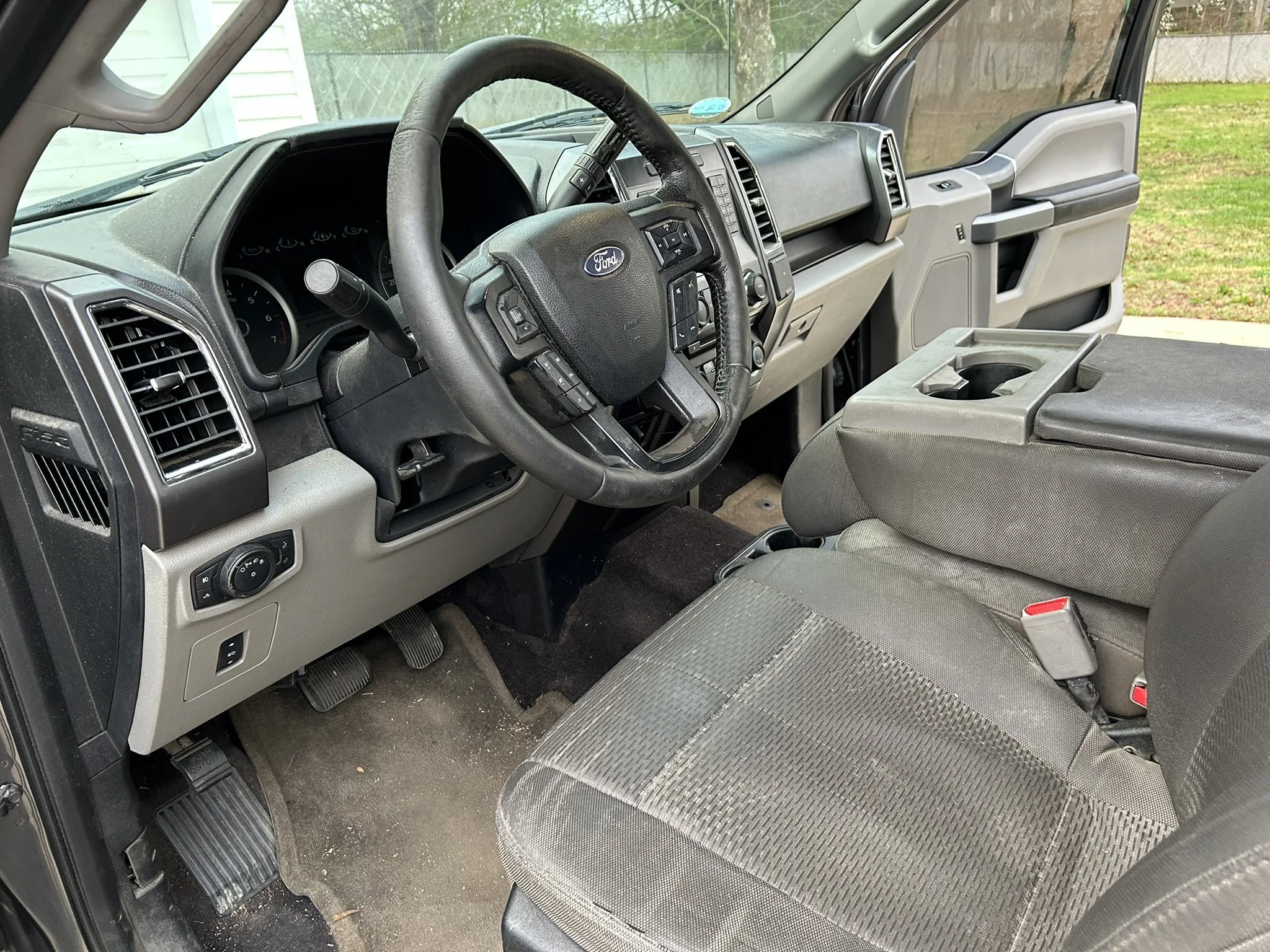 Interior of a Ford vehicle showing the driver's seat, steering wheel, dashboard, and center console with cup holder. The vehicle appears to be parked outdoors.